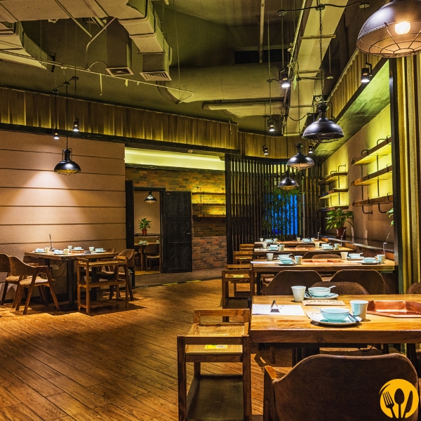 Industrialne wnętrze restauracji: odsłonięty sufit, wiszące lampy, drewniane stoliki.