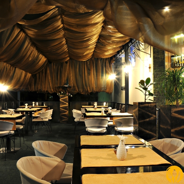 Sala restauracyjna z falistym materiałowym sufitem i przyciemnionym, nastrojowym światłem.