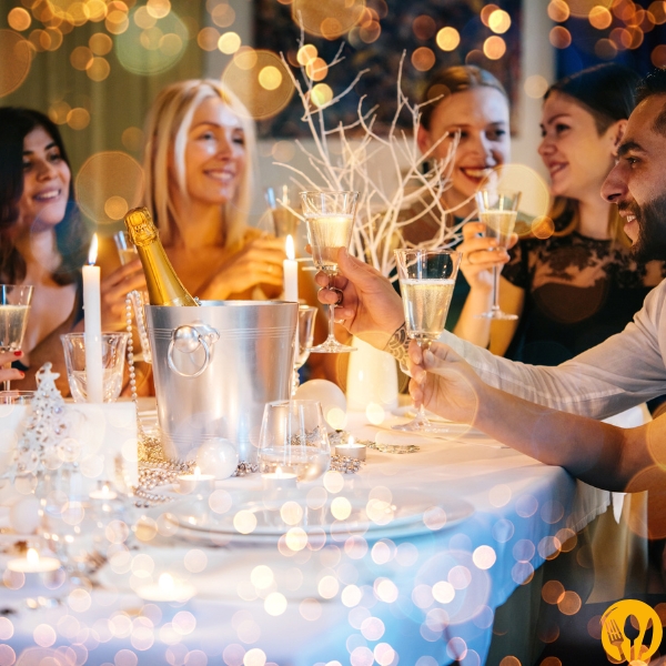 Grupa znajomych przy udekorowanym stole, kieliszki w dłoniach, ciepłe, rozproszone światło.