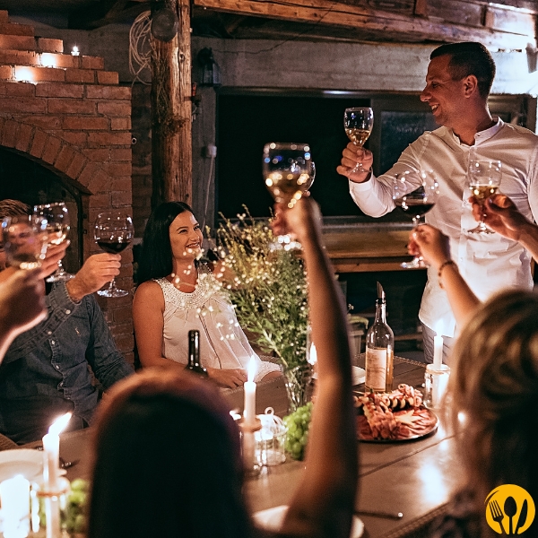 Toast przy długim stole w kameralnym wnętrzu, świece i nastrojowa kolacja.