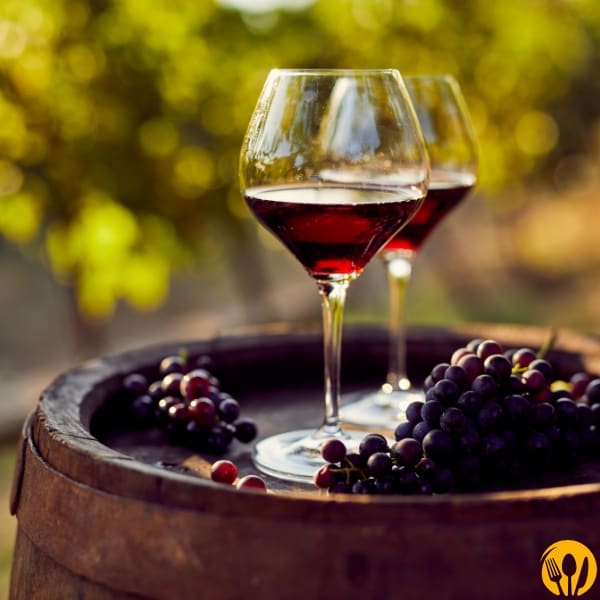 Dwa kieliszki czerwonego wina na beczce, kiście winogron w tle